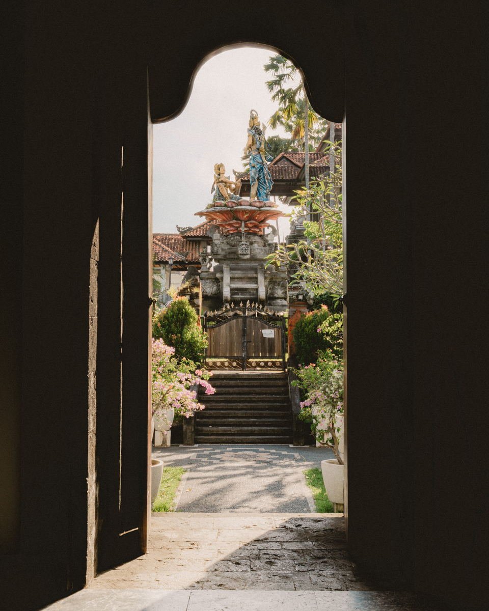Carved temple gate and bougainvillea seen through a dark open doorway, Bali
