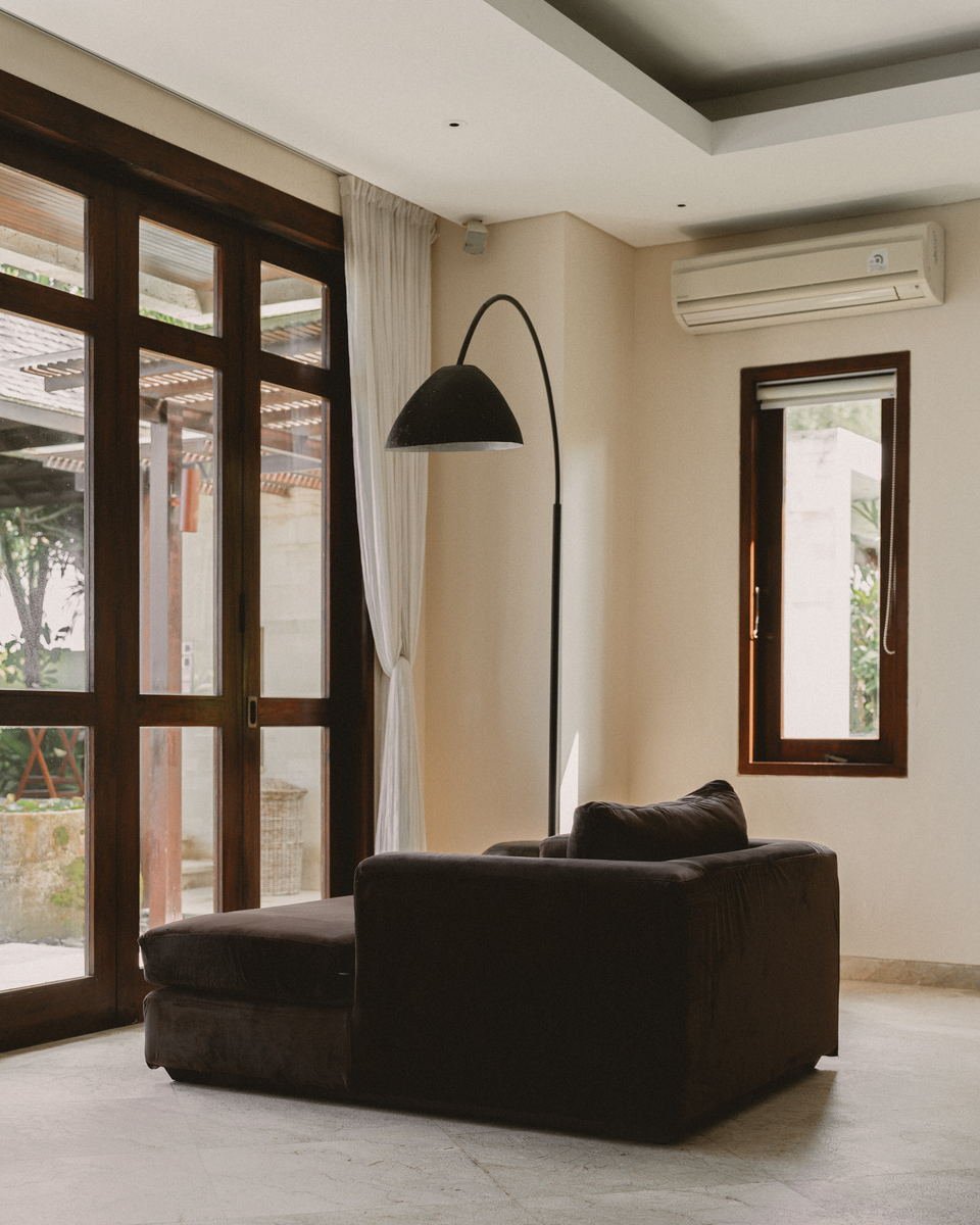Villa living room with brown velvet sofa, black arc lamp and teak framed doors