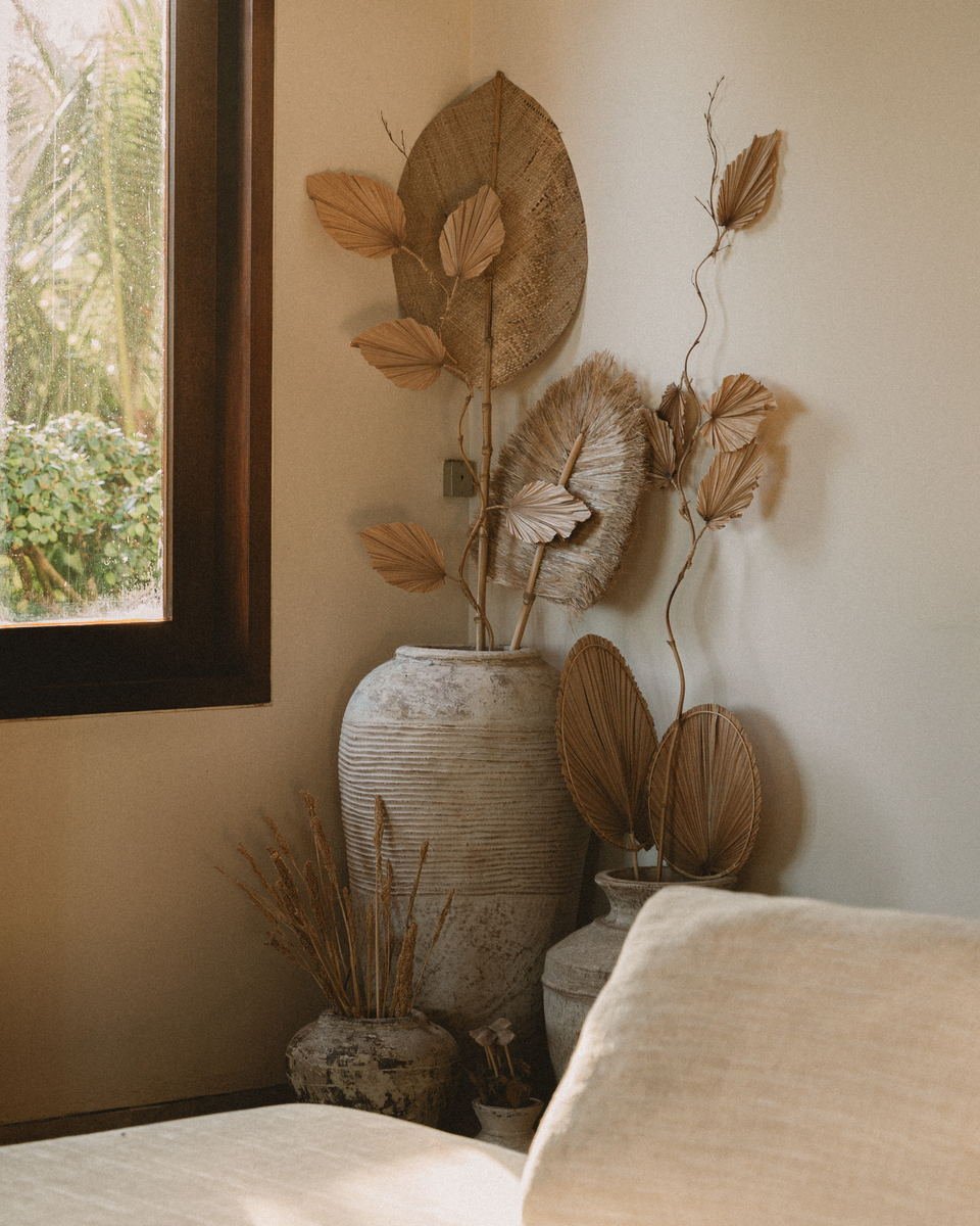 Dried palm fans and grasses in weathered stone urns beside a bedroom window