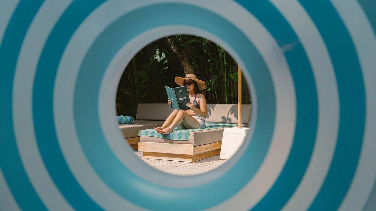 Guest reading on a daybed, framed through a blue and white striped pool ring