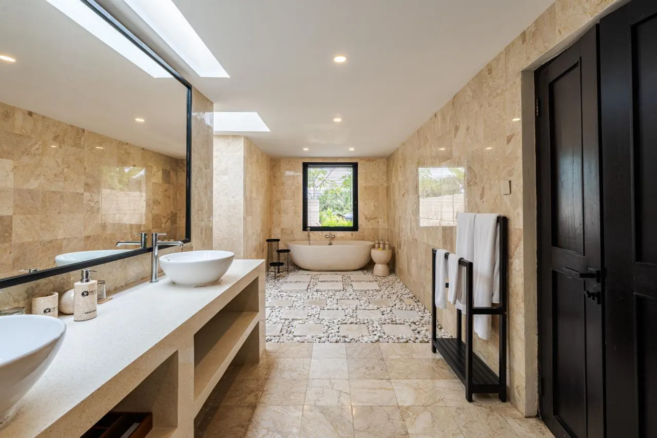 Marble bathroom with a double vanity, skylights and a freestanding stone bath on white pebbles