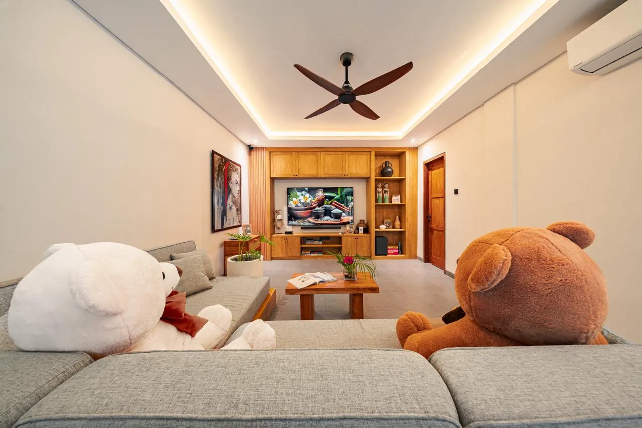 Media room with a grey sofa, two large teddy bears and a teak entertainment wall