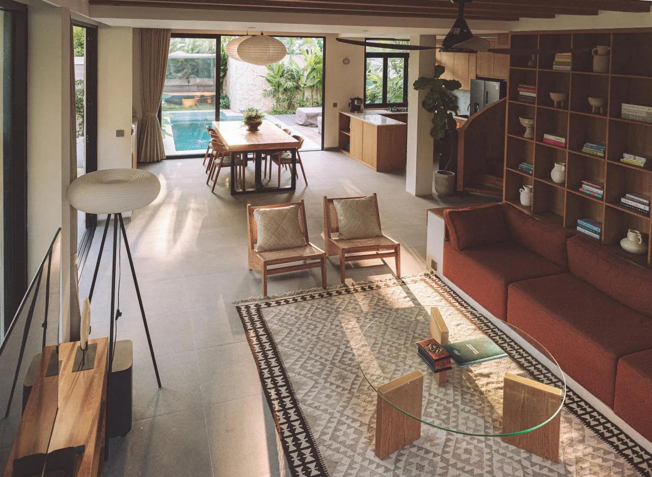 Open-plan villa living room with a terracotta sofa, rattan chairs and a dining table facing the pool