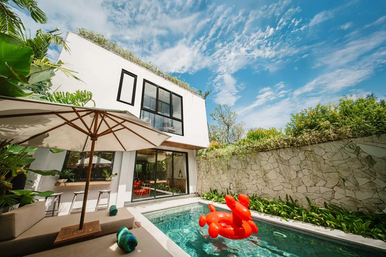 Two-storey white villa with a red inflatable in the pool, a parasol and a stone garden wall