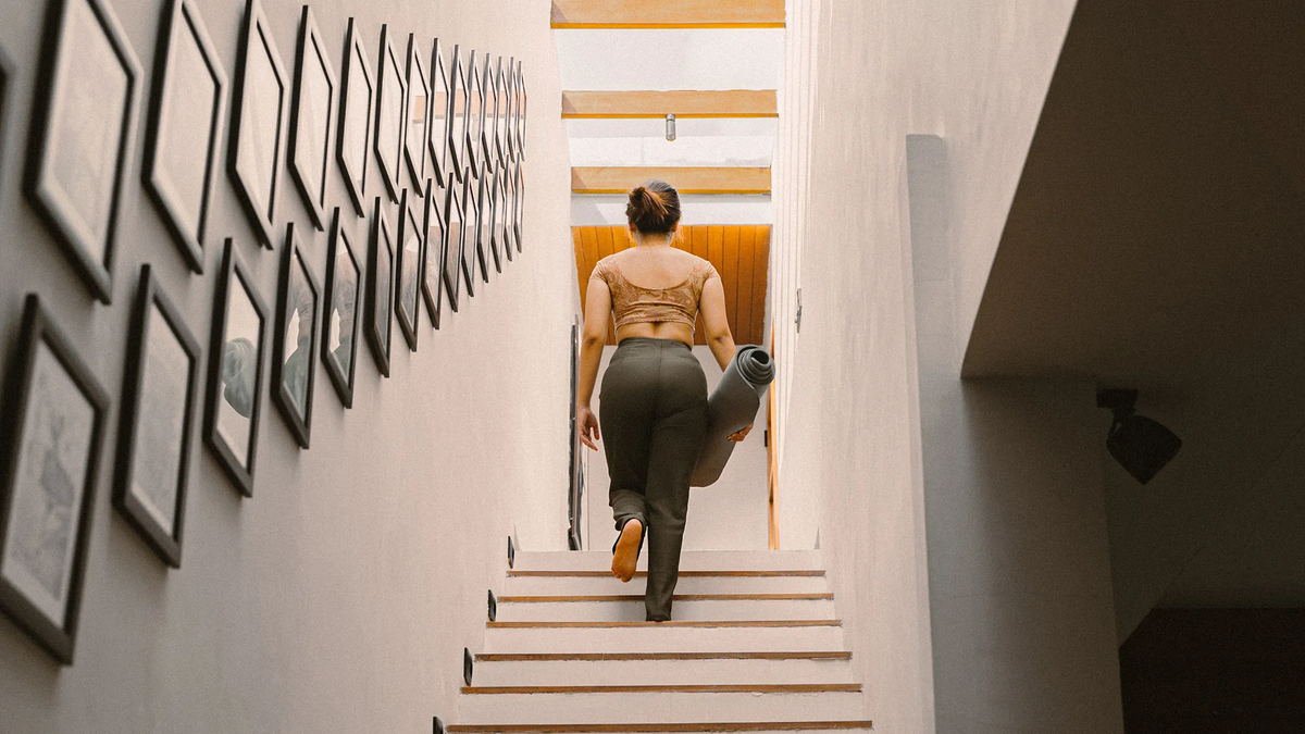 Guest carrying a rolled yoga mat up a white stair hung with black frames